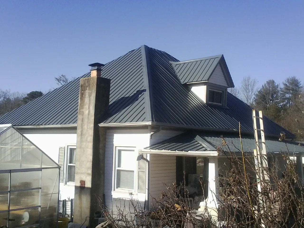 Dark blue standing seam metal roof on a white farmhouse with dormer — Slate & Tile Roof Repair by Roofing Brothers in Washington Grove