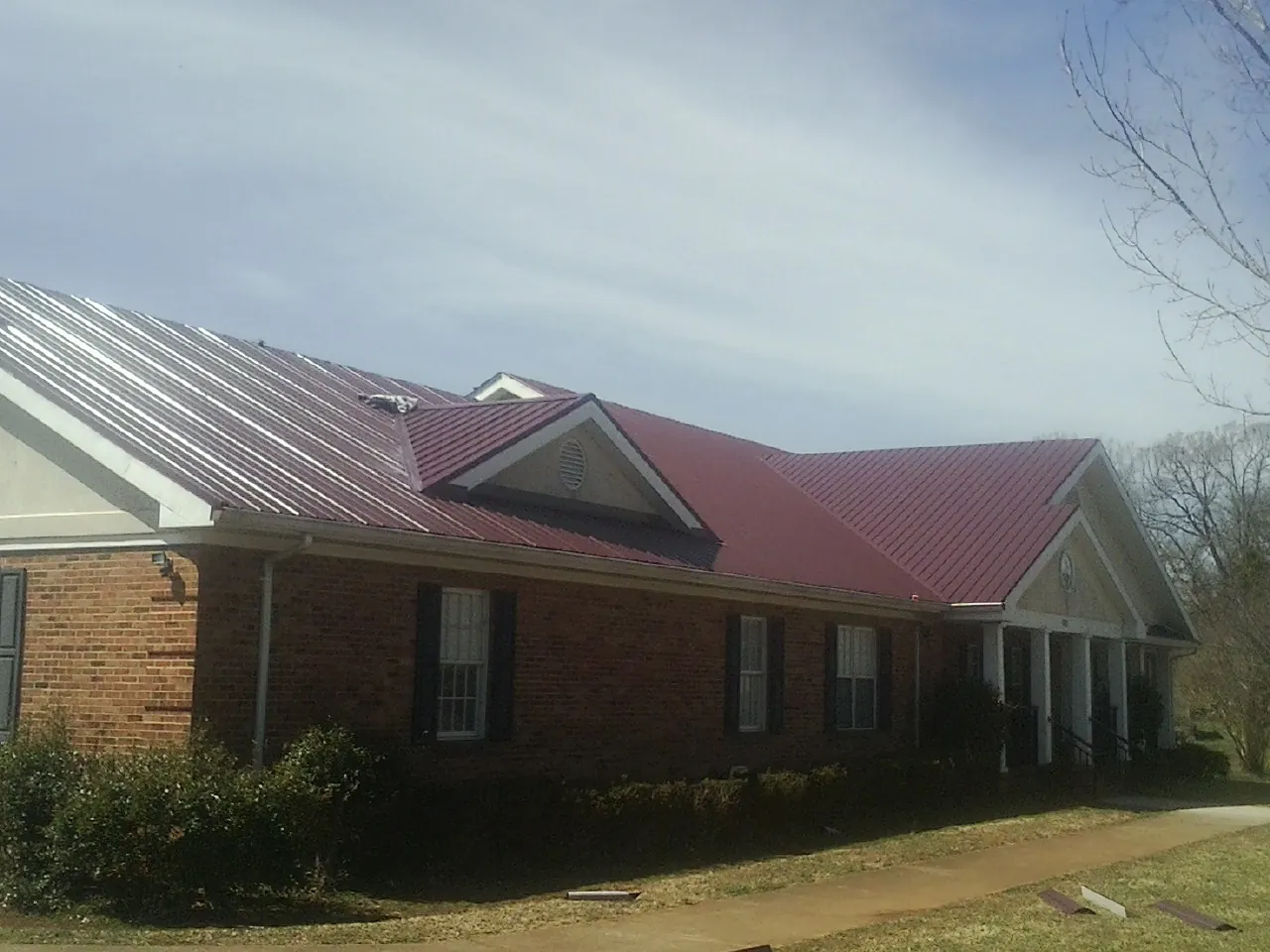 Red metal roof with gabled entries on a long brick building, from a Hail Damage Roof Repair job in Washington Grove
