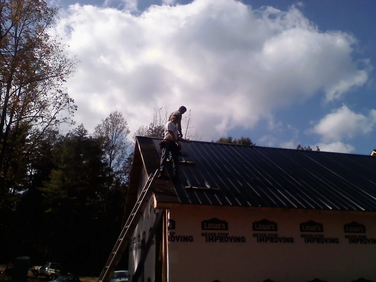 Roofer fastening dark metal panels high against a cloudy sky, from a Roof Inspection job in Washington Grove