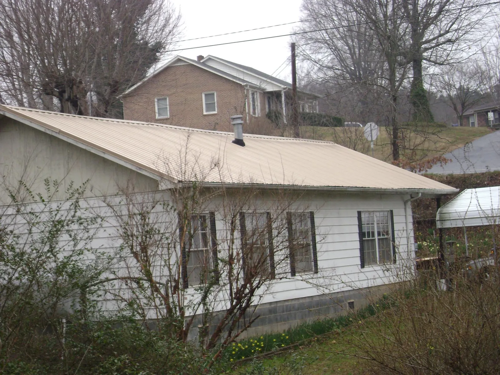 Tan metal roof on a white sided house set into a hillside — Commercial Roofing by Roofing Brothers in Washington Grove