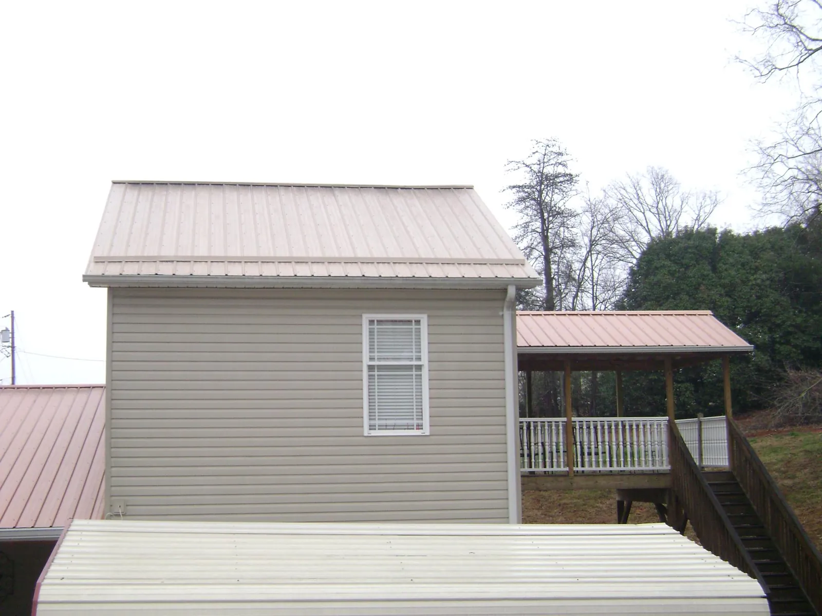 Tan metal roofs on a two story addition and attached porch, from a Roof Replacement job in Washington Grove